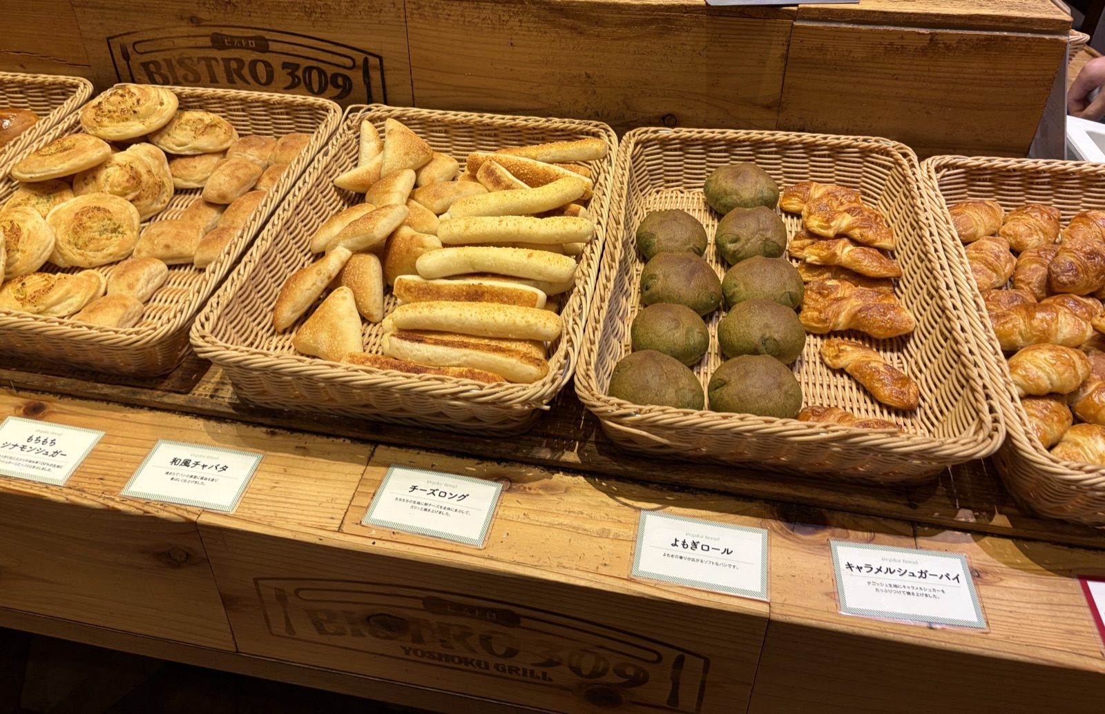 木製のカウンターに並ぶ、種類ごとのかごに入った焼きたてパン。手前にはパン名を書いた札が並んでいる